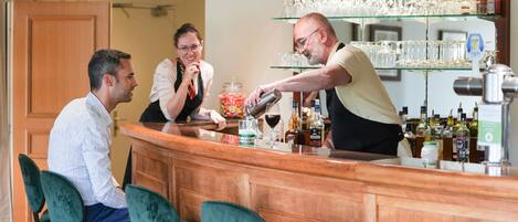 A bar area with a wooden counter, green bar stools, and a glass display shelf with multiple glasses.