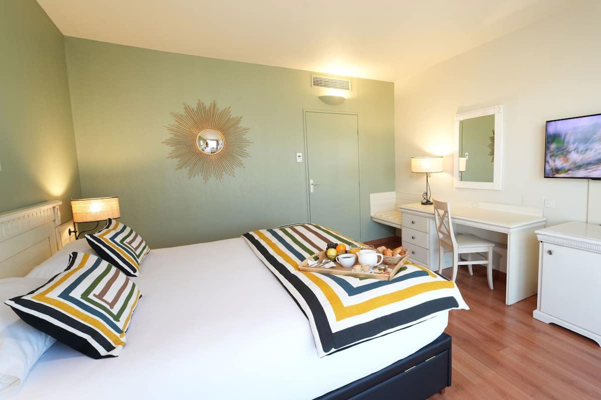 A hotel room with a bed, bedside lamps, a desk, a chair, a television, and a wall-mounted mirror.