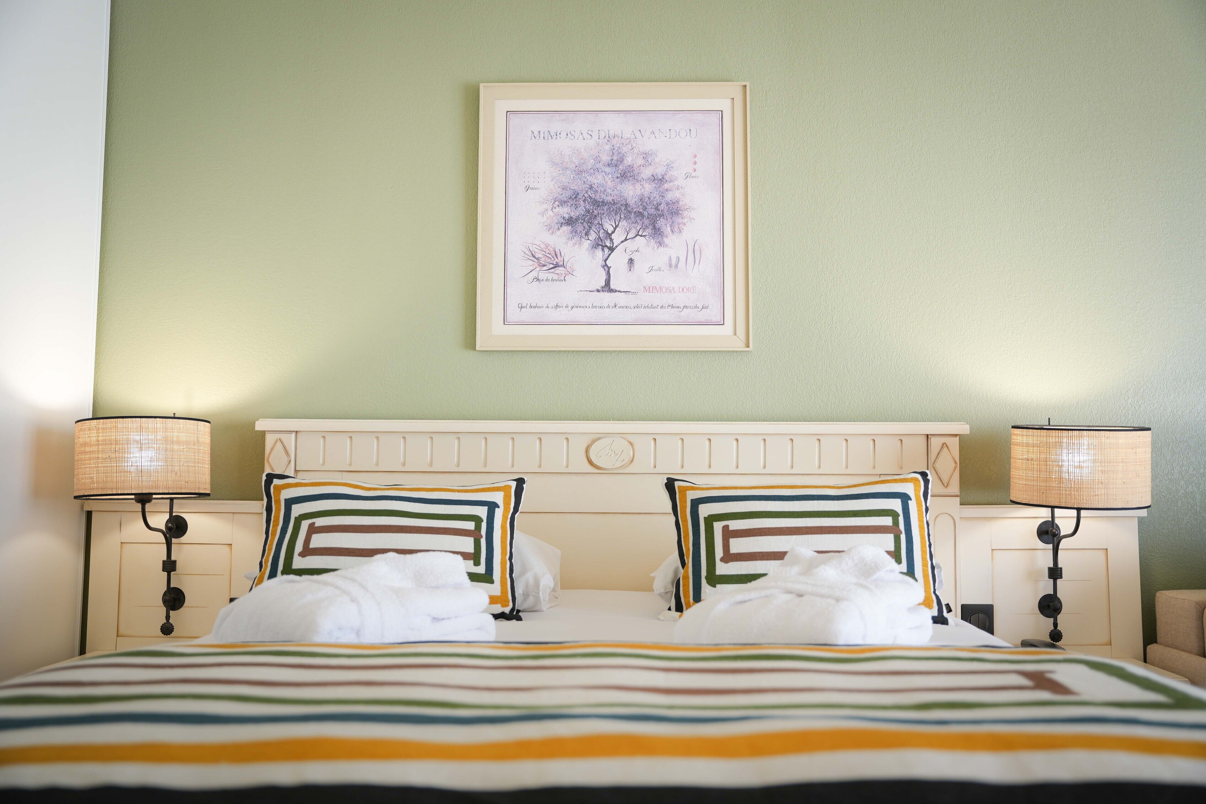 A neatly made double bed with striped bedding, two bedside lamps, and a framed picture on the wall.