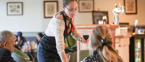 Eine Person serviert Wein an eine sitzende Person in einem Restaurant.