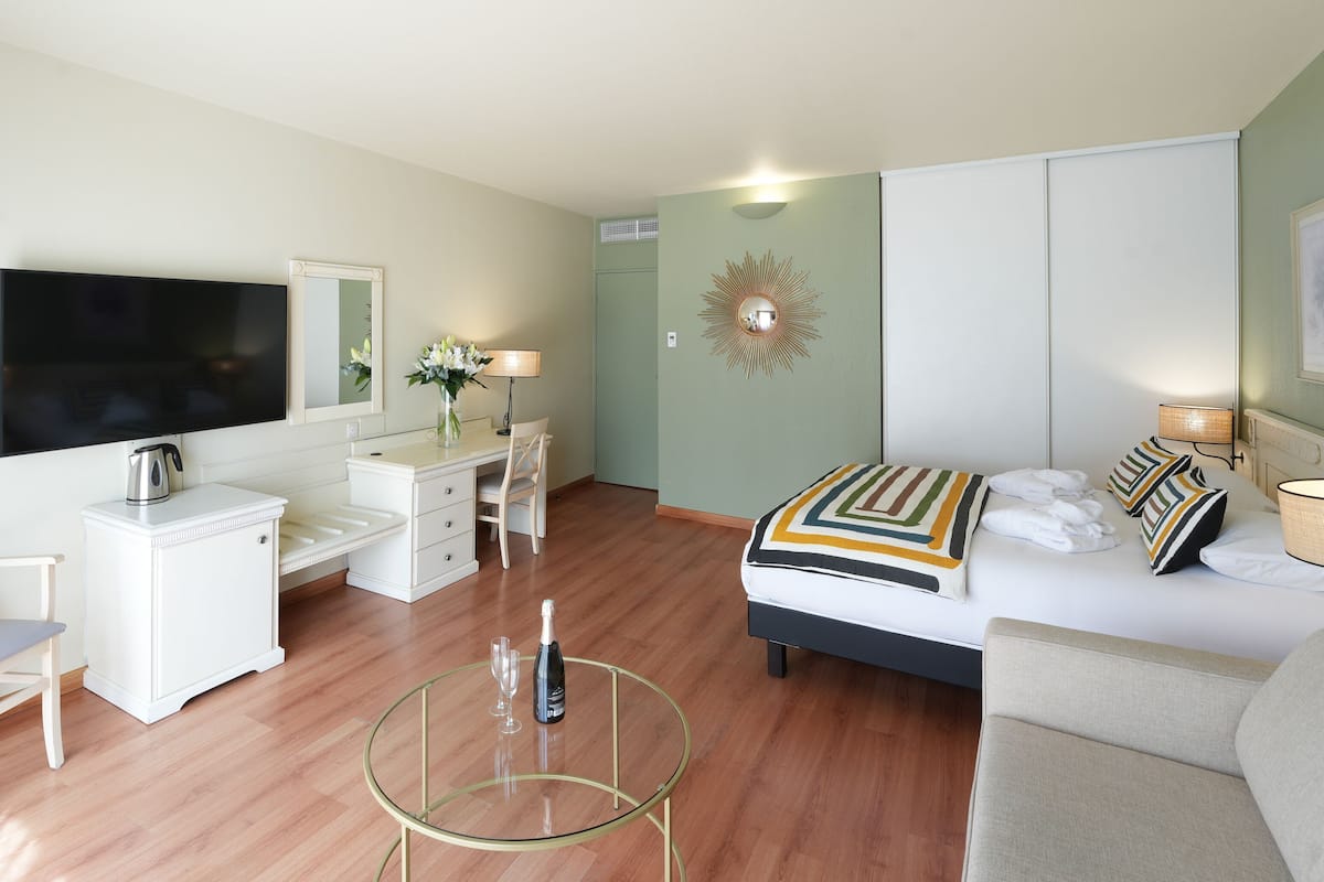 A modern hotel room with a bed, sofa, TV, desk, and a glass coffee table.