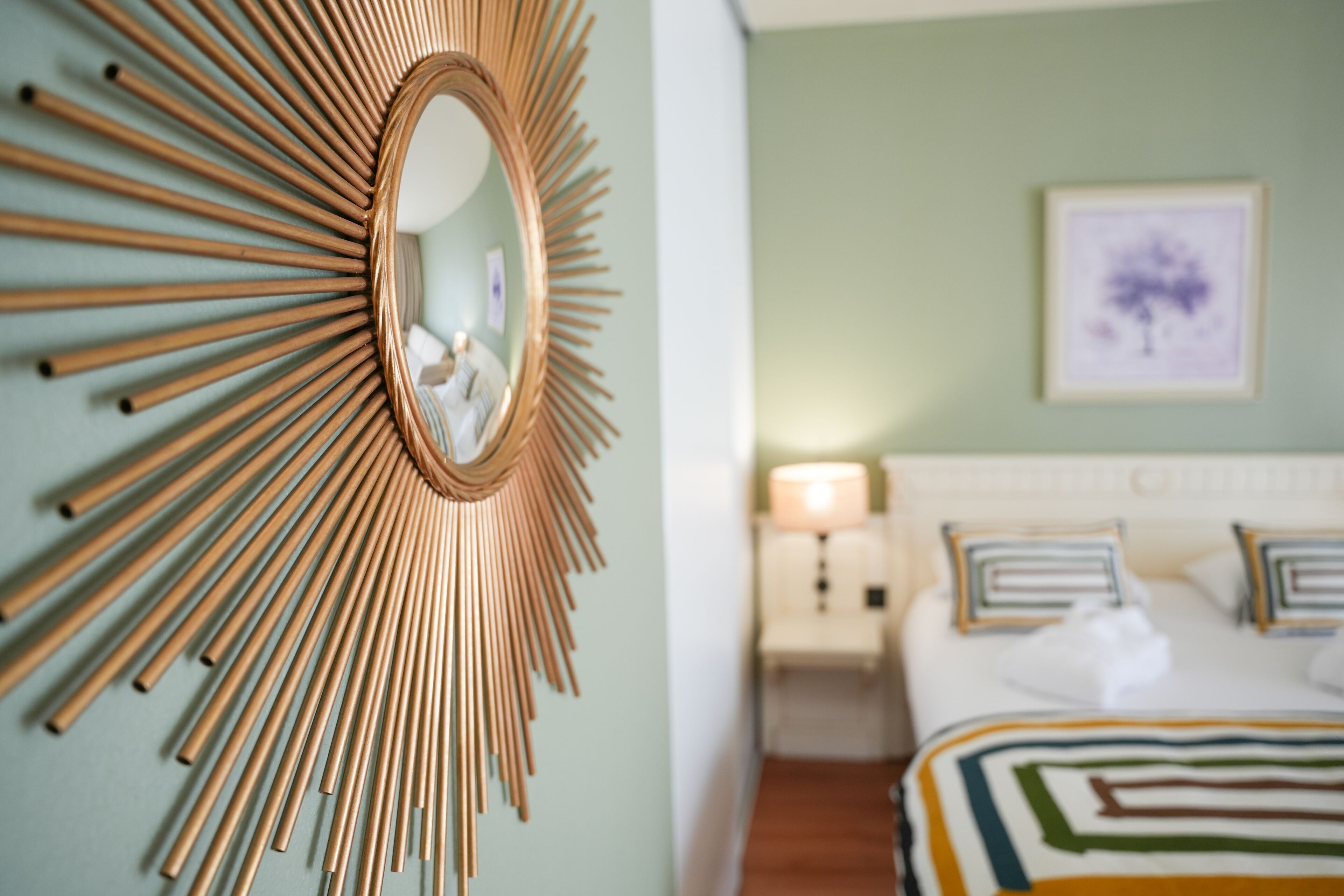 A room with a sunburst mirror, a bed with striped bedding, and a framed picture on the wall.