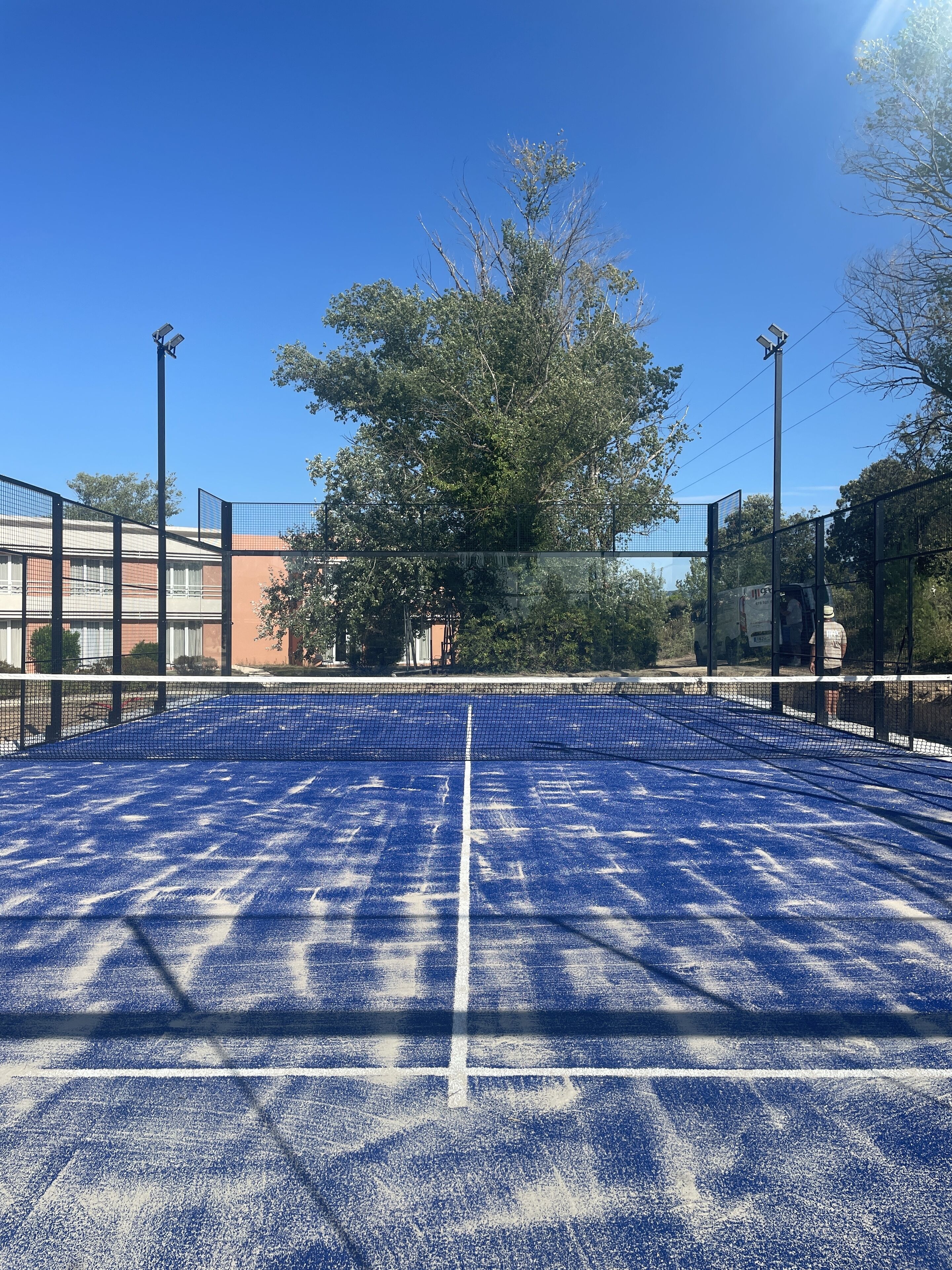 Una cancha de tenis con red, rodeada por una valla y árboles.