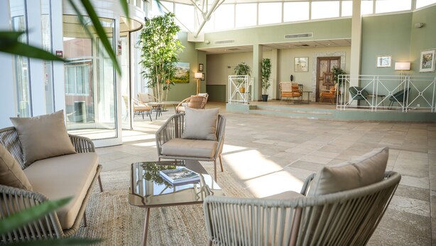 Un amplio espacio interior con muebles de mimbre, una mesa de centro de cristal y vistas a través de amplias ventanas.