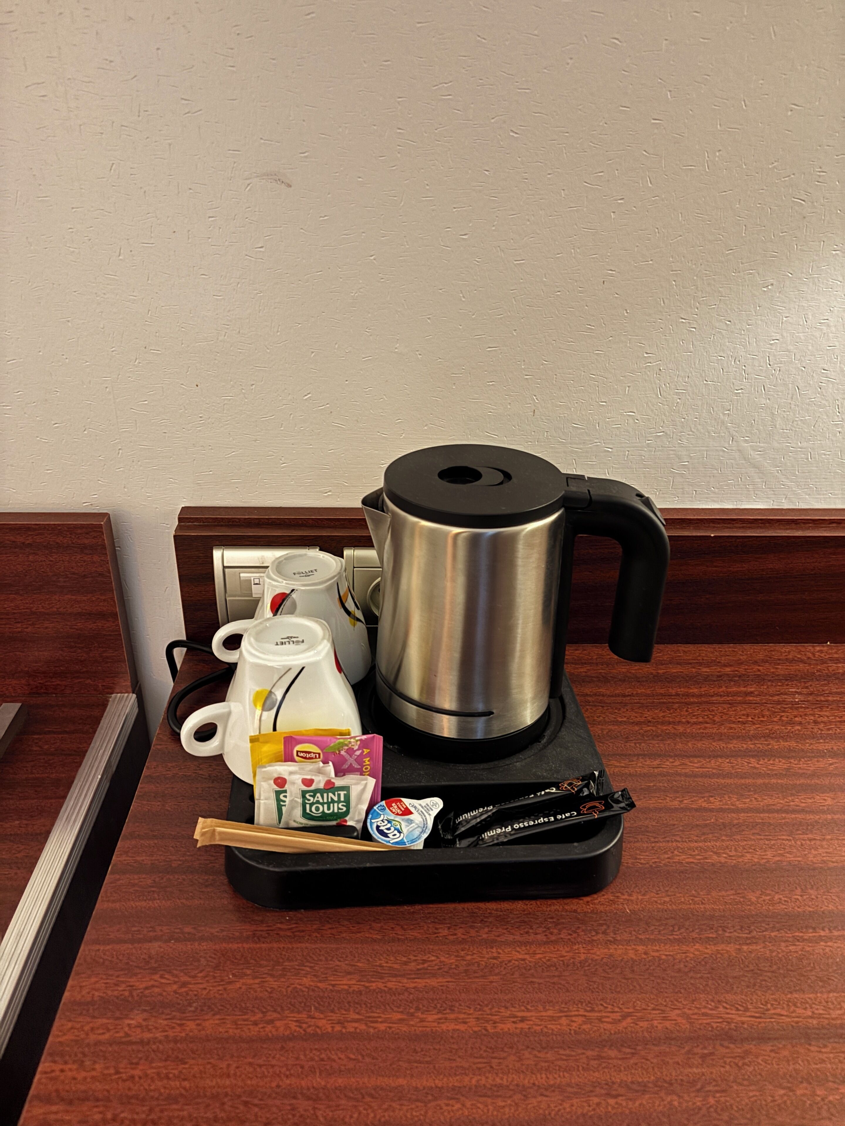Una estación de café con una cafetera, una jarra de leche, un sobre de azúcar y un sobre de crema en una bandeja.
