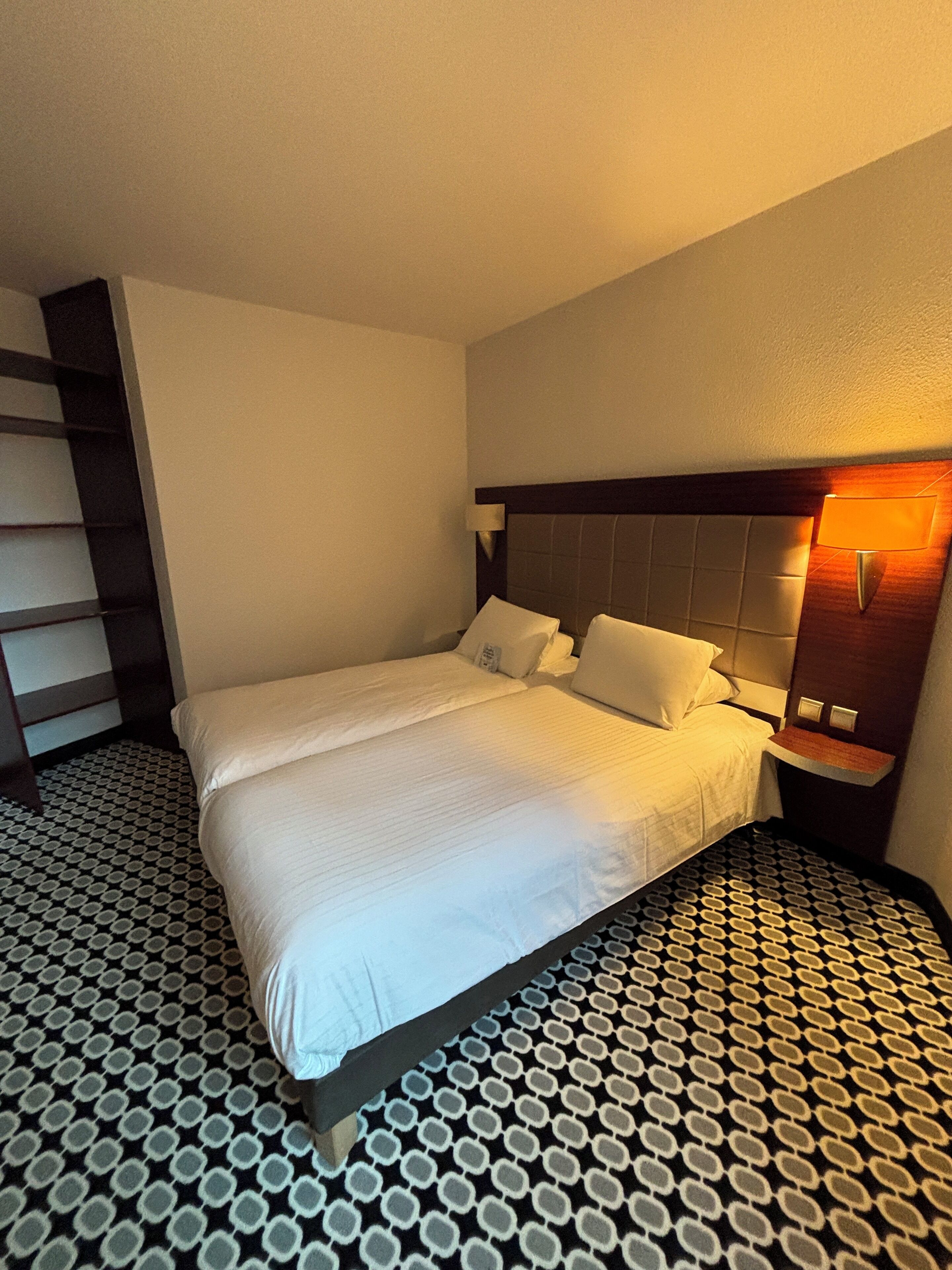A hotel room with a bed, a nightstand, a lamp, and a patterned floor.