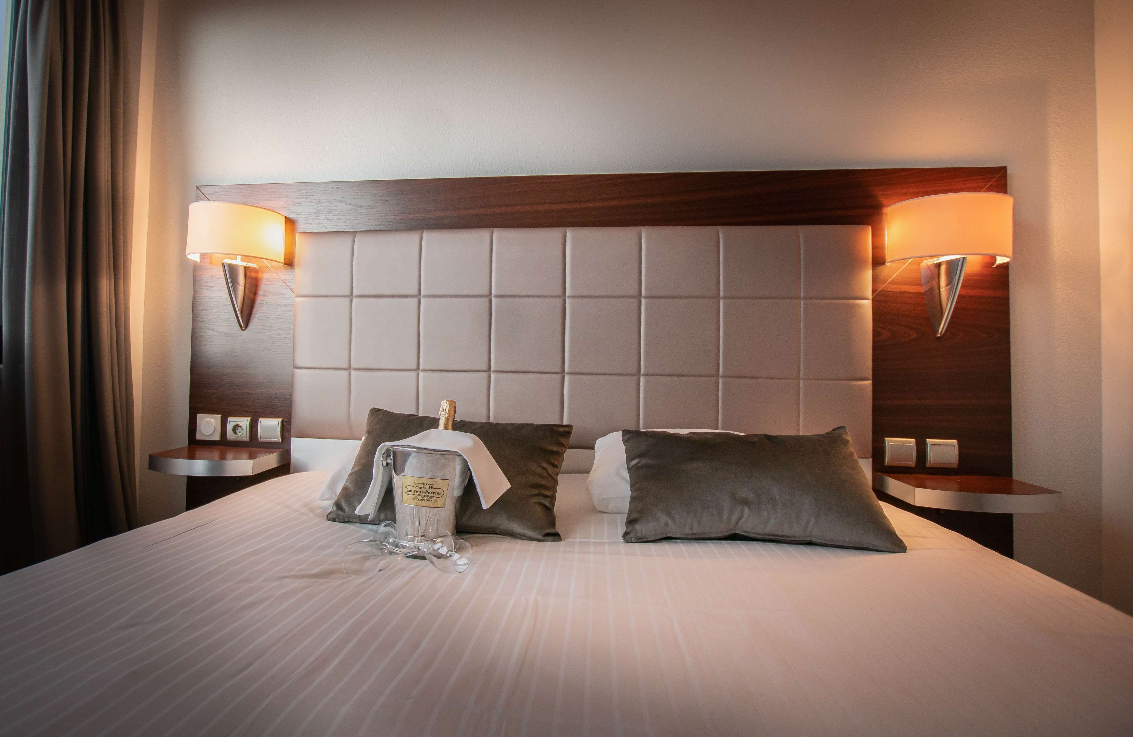 Habitación de hotel con una cama grande, dos mesitas de noche, un cabecero y dos lámparas fijadas a la pared.