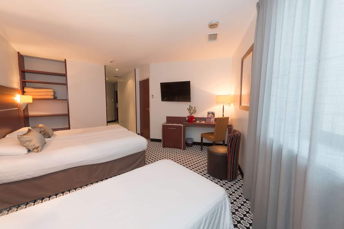 A hotel room with two beds, a desk, a chair, a TV, and a bathroom.