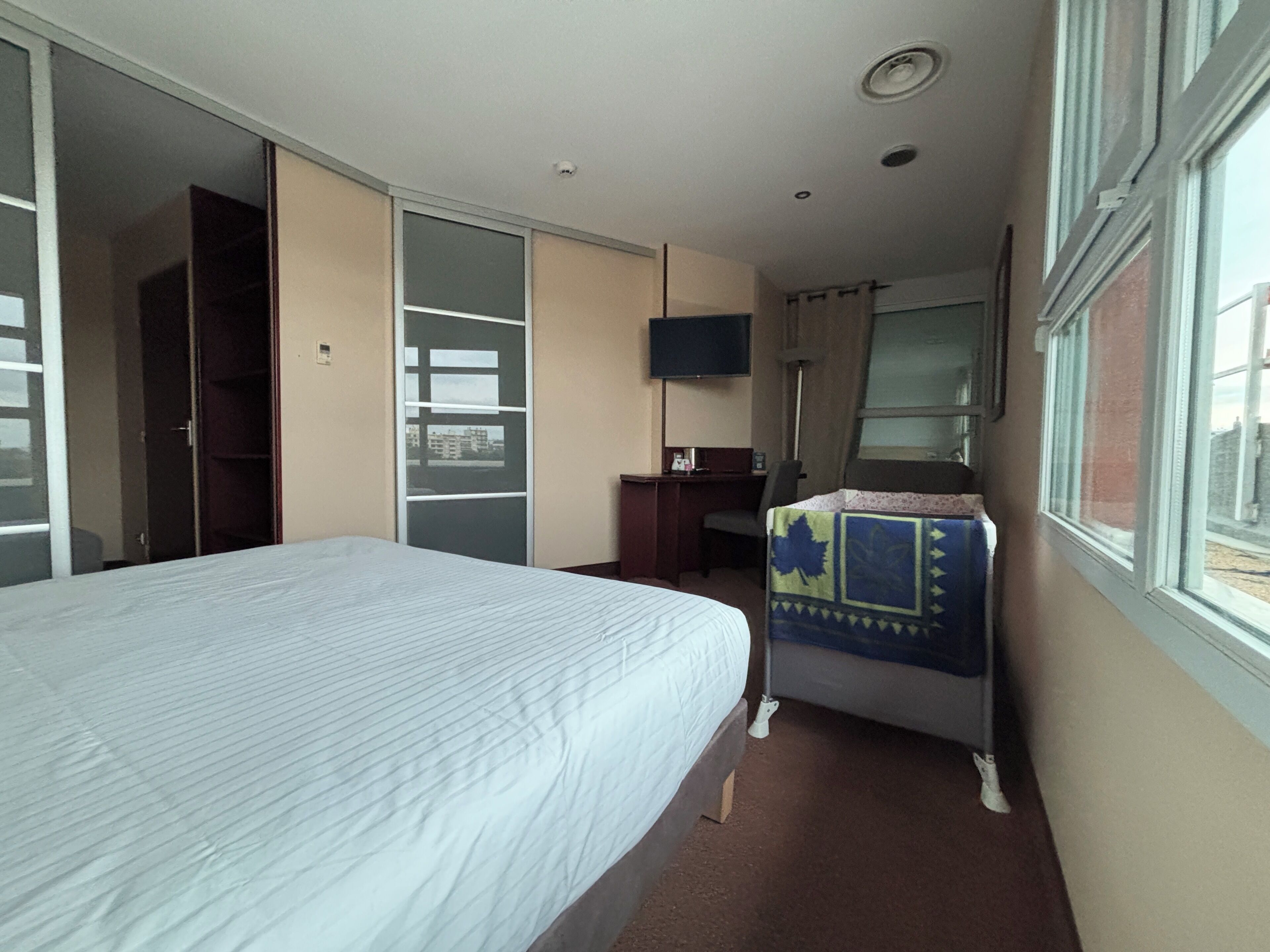 A hotel room with a bed, a desk, a chair, a TV, and a window with a view.