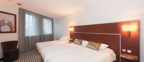 Habitación de hotel con dos camas, un ventanal con cortinas, una lámpara de pared y un suelo estampado.