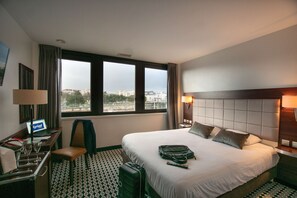 A hotel room with a large bed, a desk with a laptop, a chair, and a suitcase.