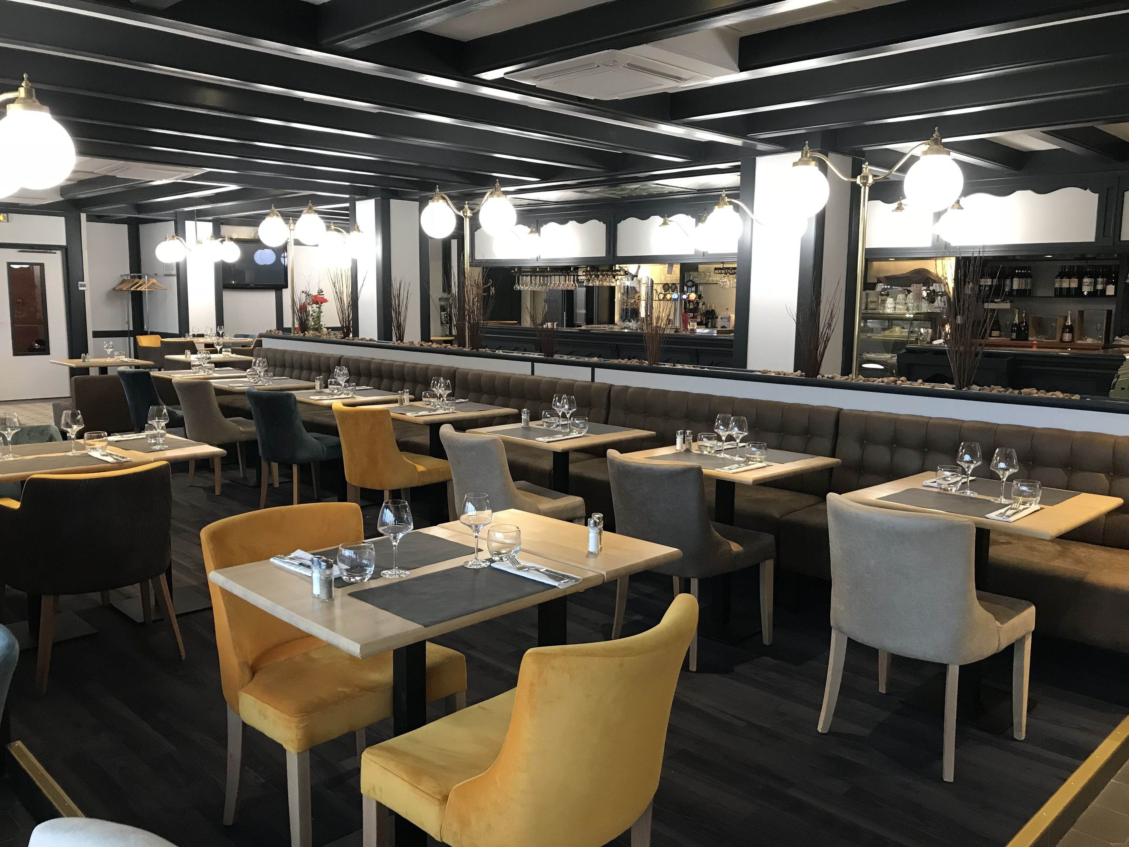 A modern restaurant interior with multiple dining tables and chairs, a bar area, and a view of the street outside.