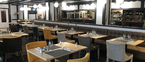 Un interior de restaurante moderno con varias mesas y sillas, una zona de bar y vistas a la calle.