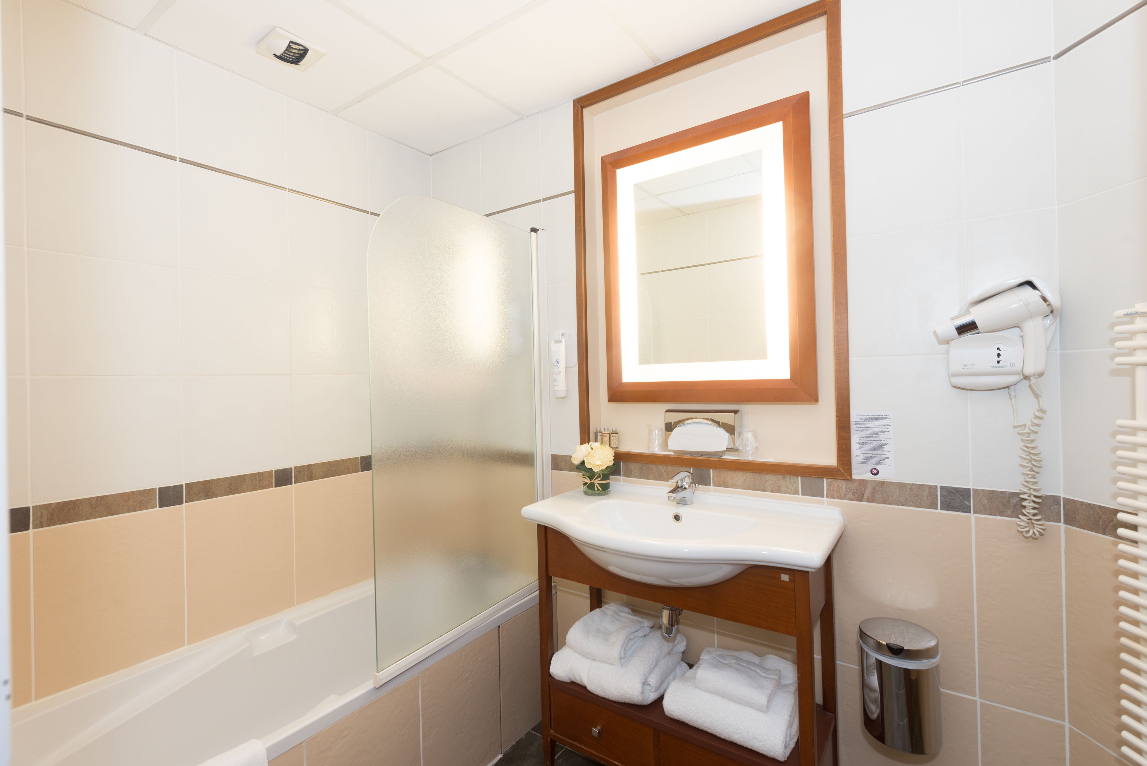 A bathroom with a bathtub, a sink, a mirror, a trash can, and a hairdryer.