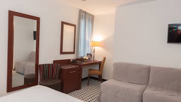 A hotel room with a bed, a desk with a chair, a sofa, a mirror, a lamp, and a television.