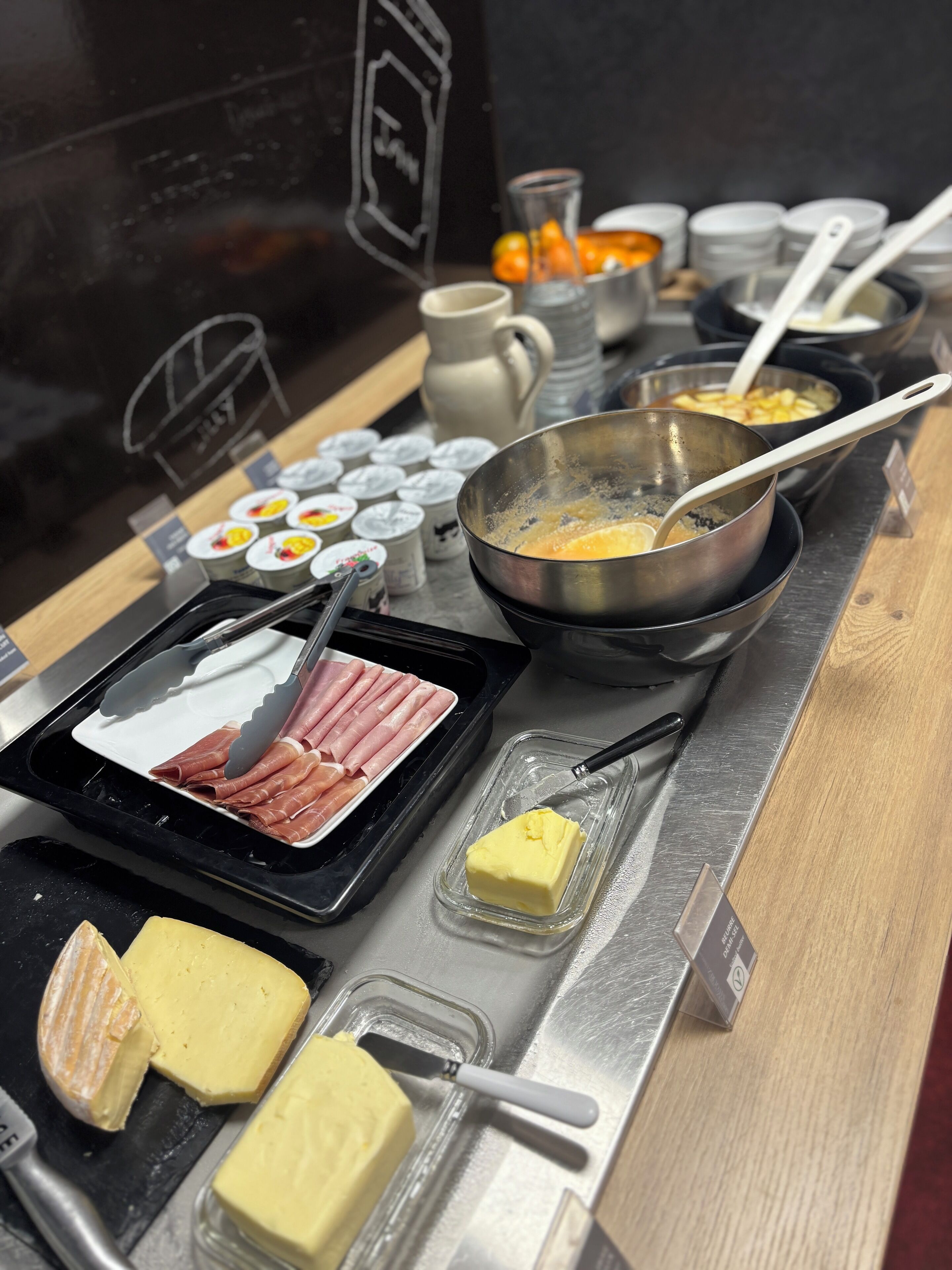 A buffet setup with various food items including meats, cheeses, and a bowl of eggs being cooked.