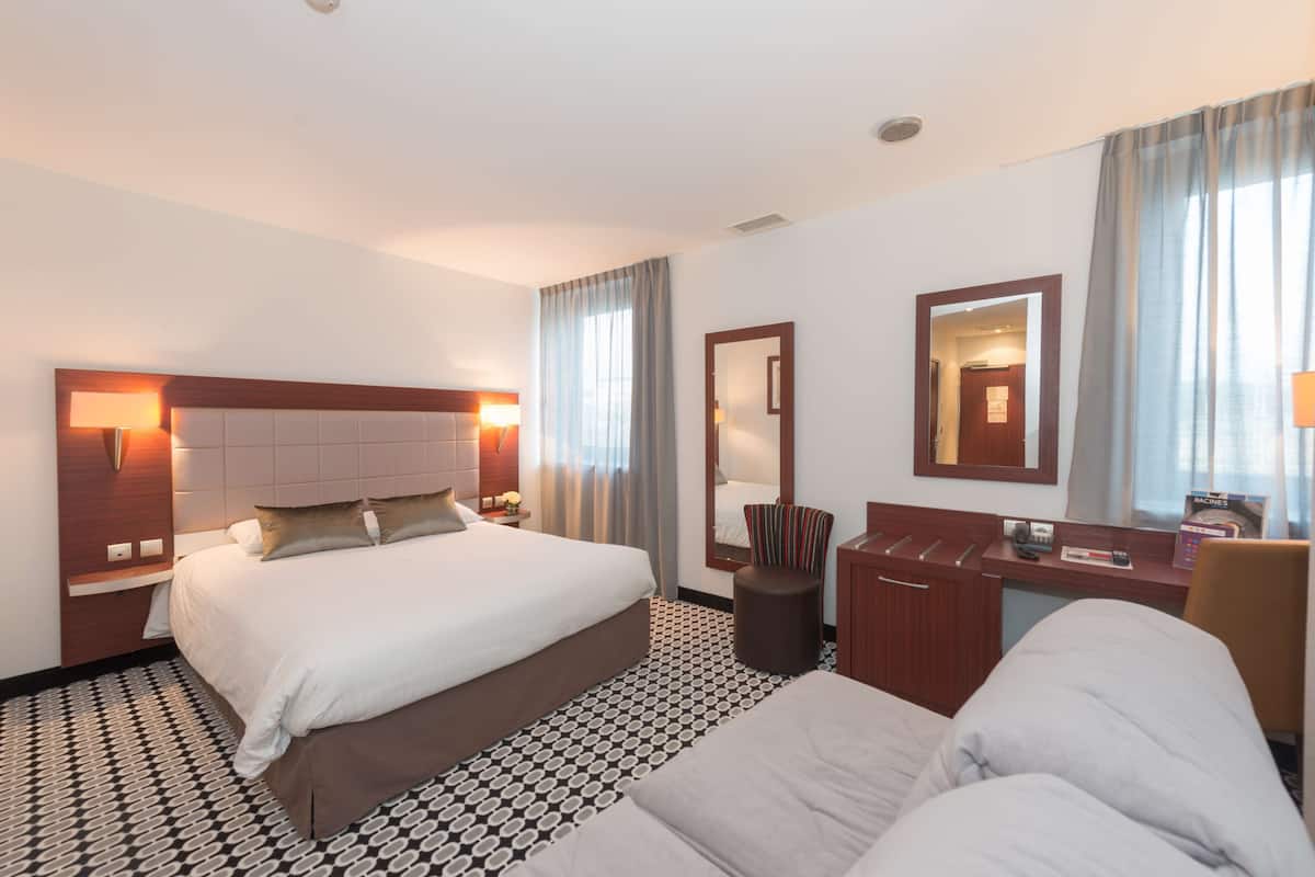 A hotel room with a large bed, a desk, a chair, a mirror, and a small stool.