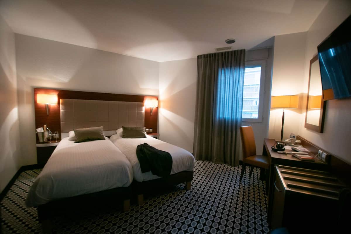A hotel room with two beds, a desk, a chair, and a window with curtains.
