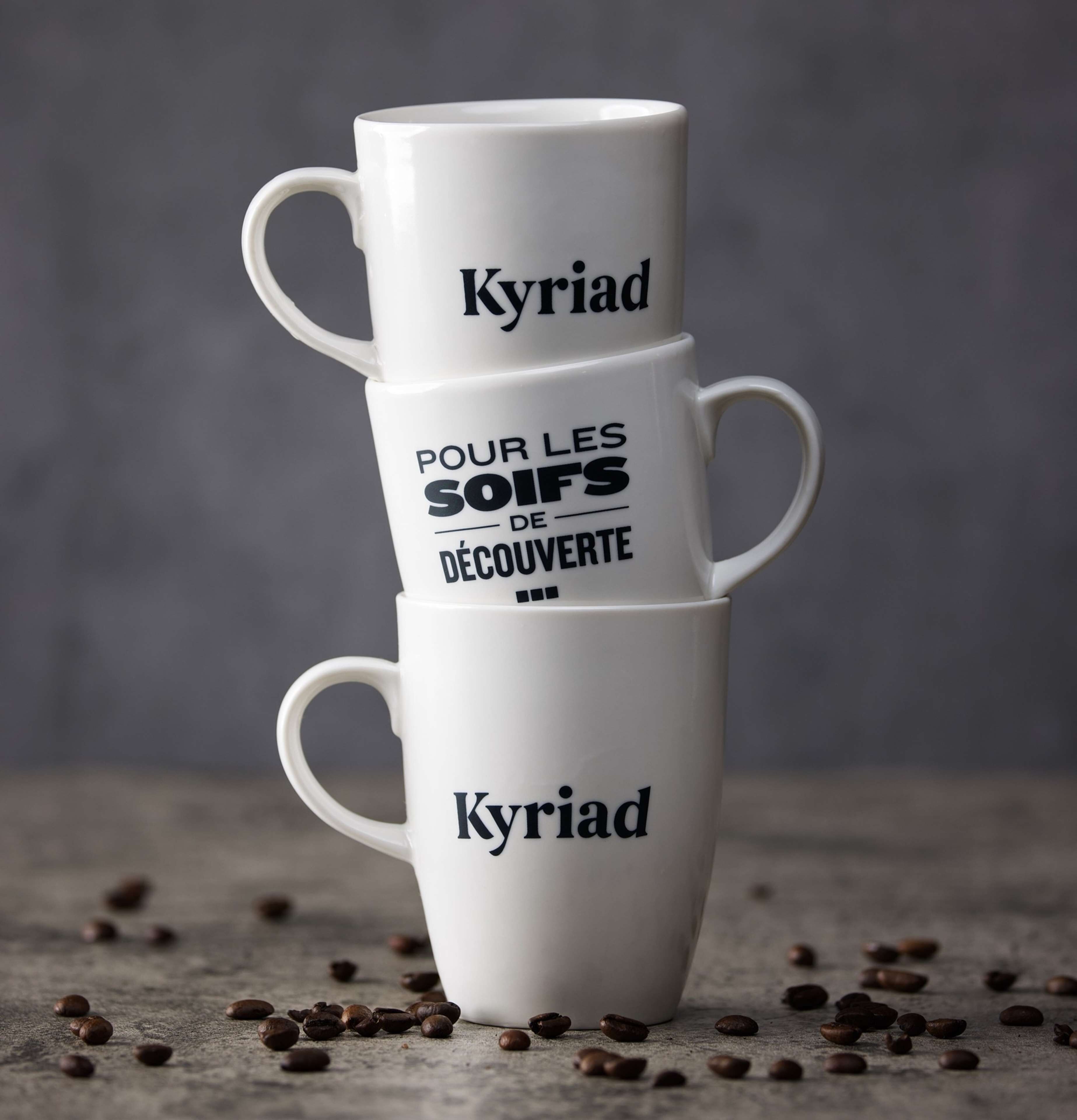 Three stacked white coffee cups with text, placed on a surface with scattered coffee beans.