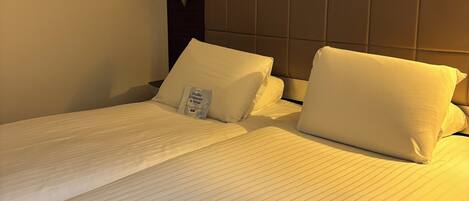Une chambre d’hôtel avec deux lits, chacun doté de draps et d’oreillers blancs, d’une tête de lit sombre et d’une lampe de chevet.