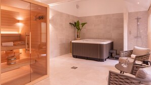 Een moderne badkamer met een sauna, een jacuzzi en een zithoek met een plant.