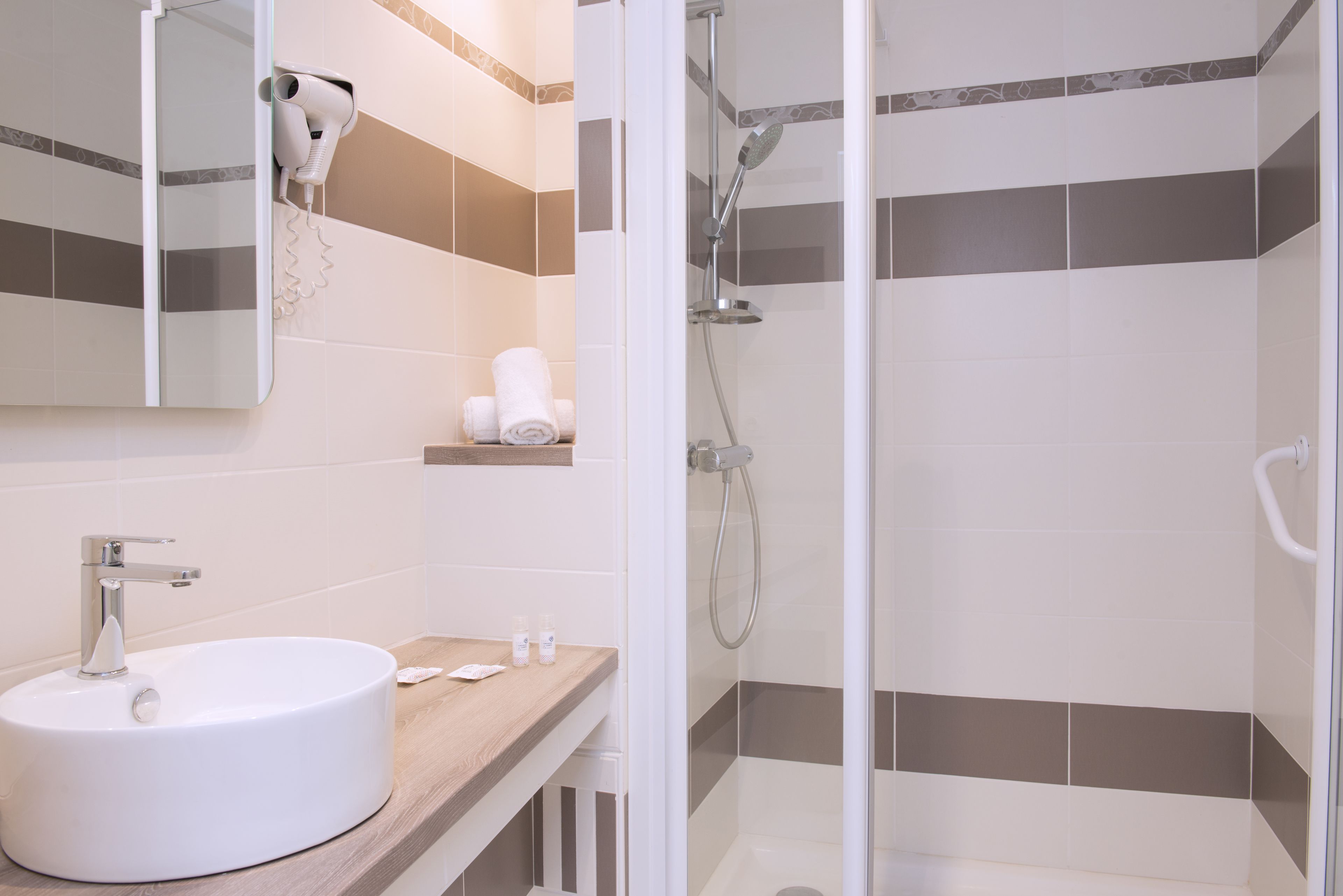 Un bagno moderno con un lavandino rotondo, uno specchio, un asciugacapelli e una doccia con porta in vetro.