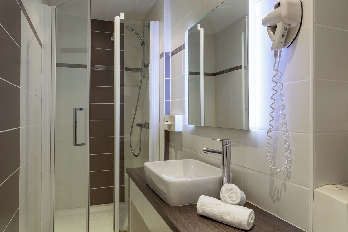 Een moderne badkamer met een douchecabine van glas, een wit wastafelmeubel en een haardroger die aan de muur is bevestigd.