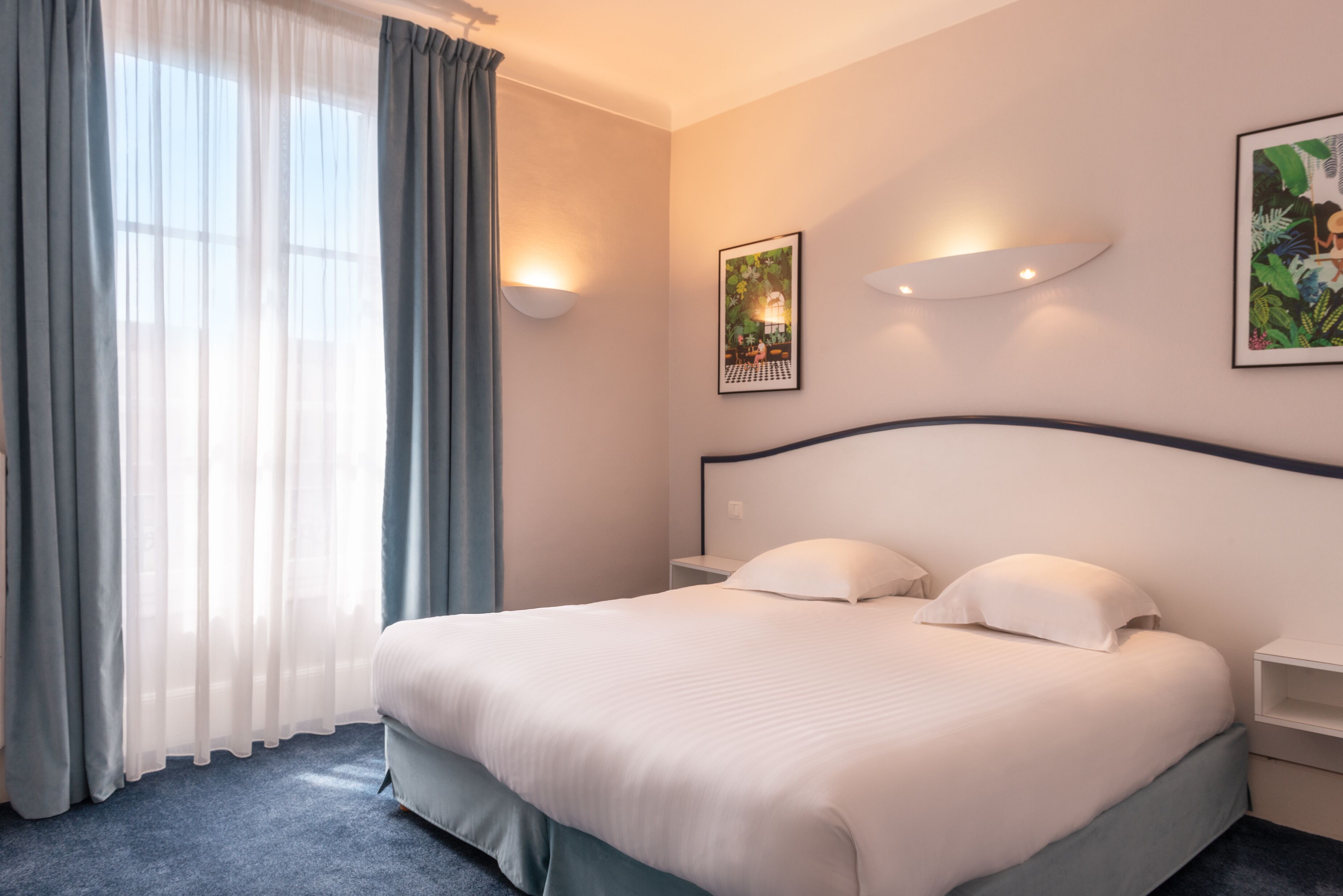 A hotel room with a large bed, a bedside table, a nightstand, and a window with curtains.