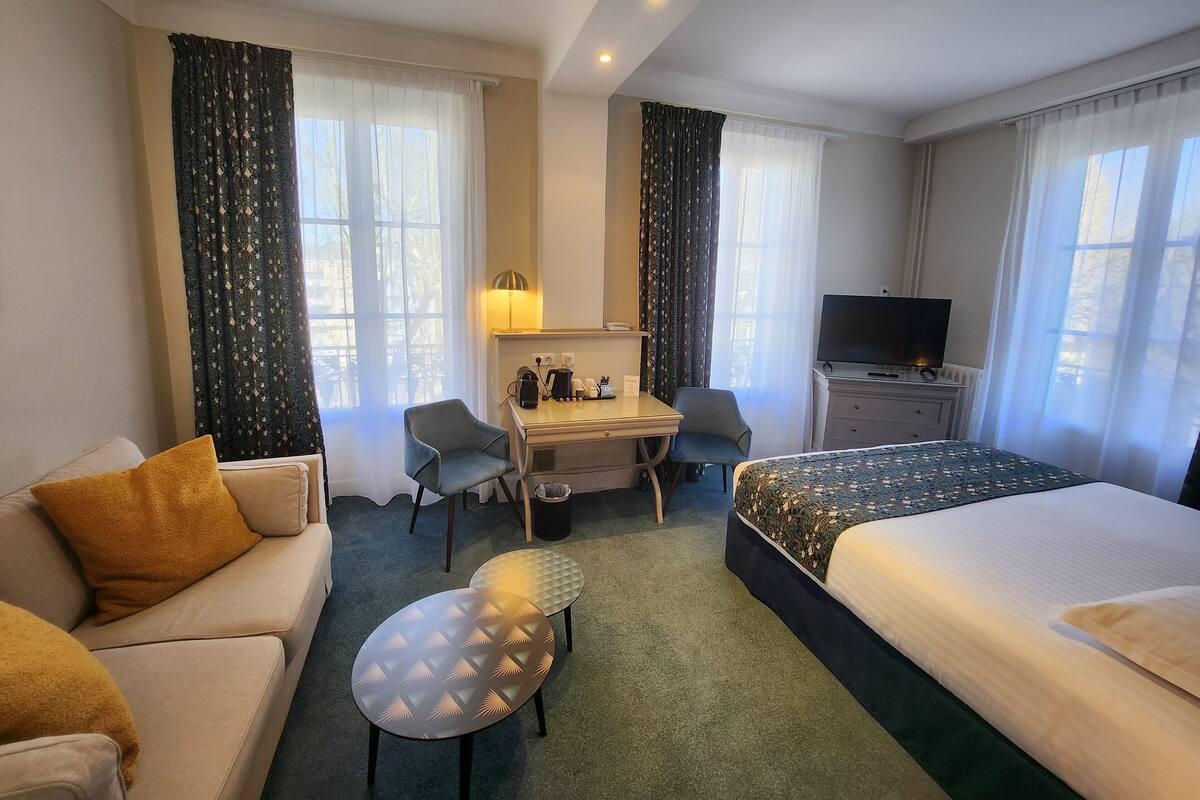 Une chambre d’hôtel comprenant un lit, un bureau, deux chaises, une télévision et un canapé.