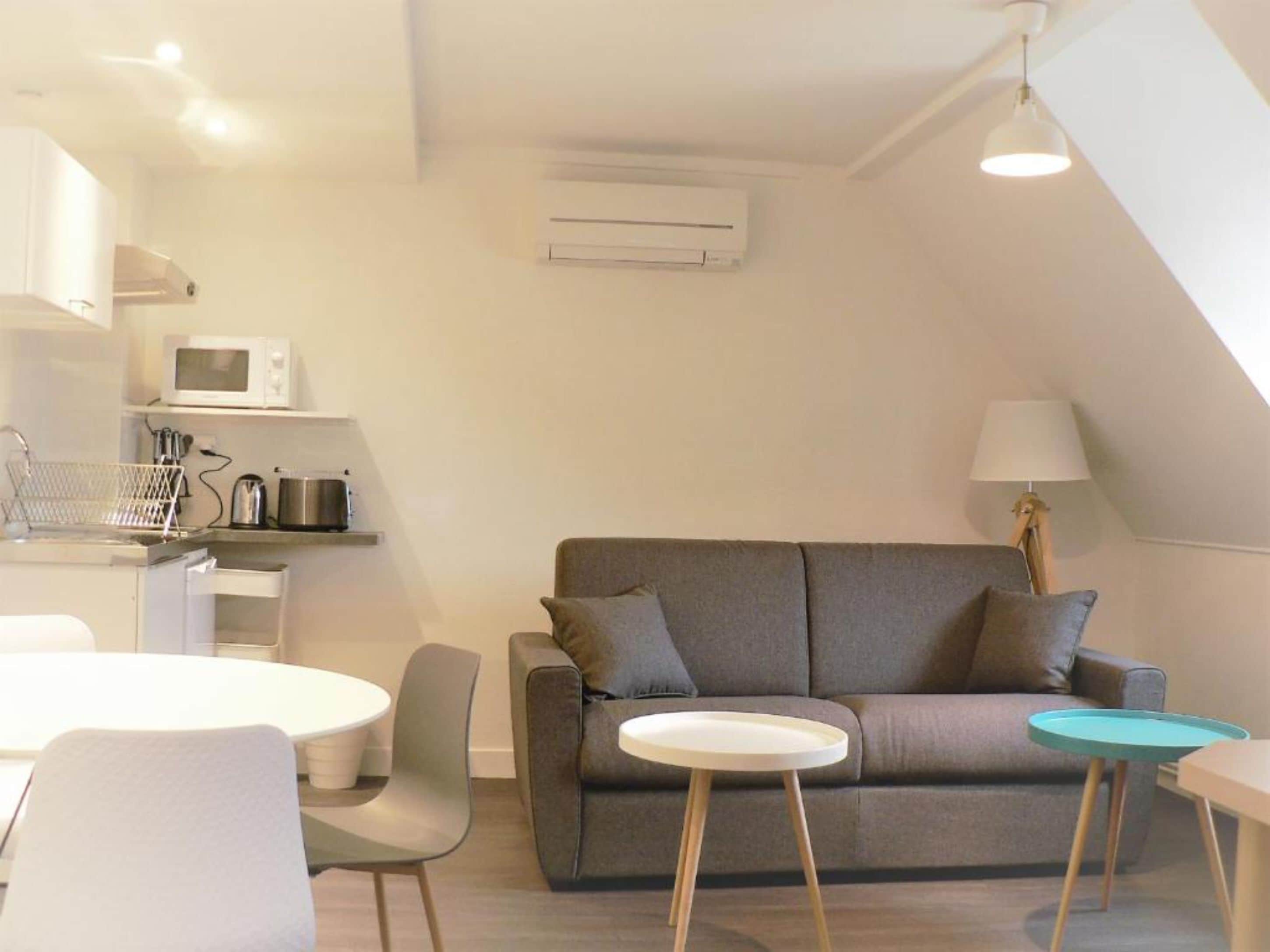 A modern living space with a grey sofa, a small round table, and a dining area with a white table and chairs.
