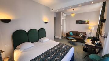 Quarto de hotel com uma cama grande, um sofá, uma mesinha e uma escrivaninha com cadeira.