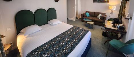 A hotel room with a large bed, a sofa, a small table, and a desk with a chair.