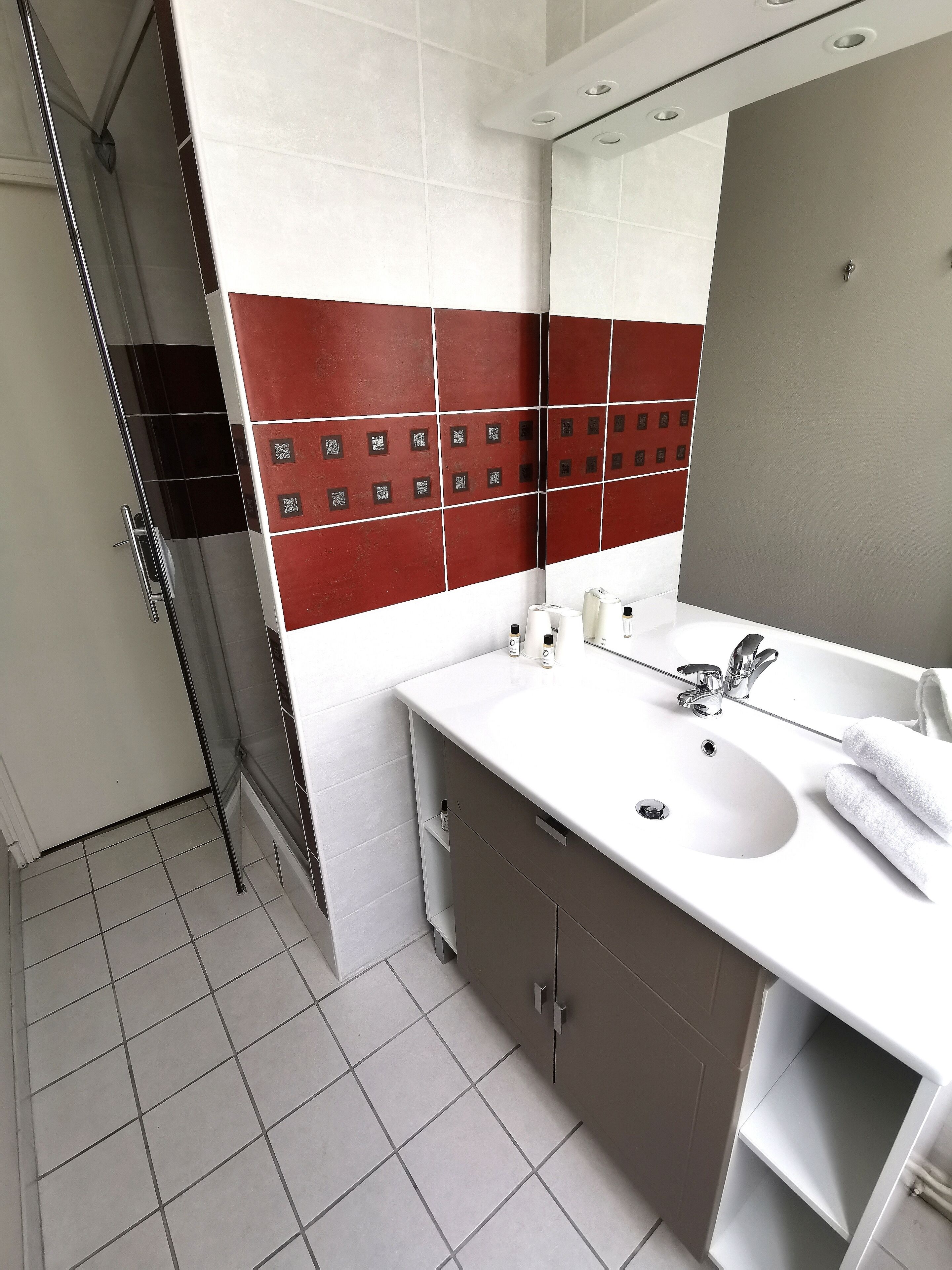 Une salle de bain moderne avec un lavabo blanc, un miroir et un mur recouvert de carreaux rouges.