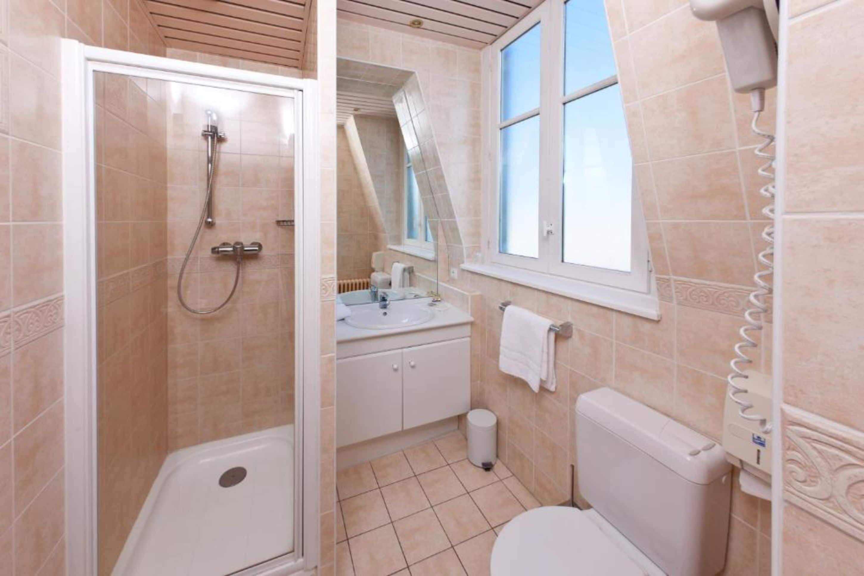 A bathroom with a shower, toilet, sink, and window.