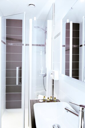 Une salle de bain moderne dotée d’une douche à l’italienne, d’un grand miroir et d’un meuble-lavabo.