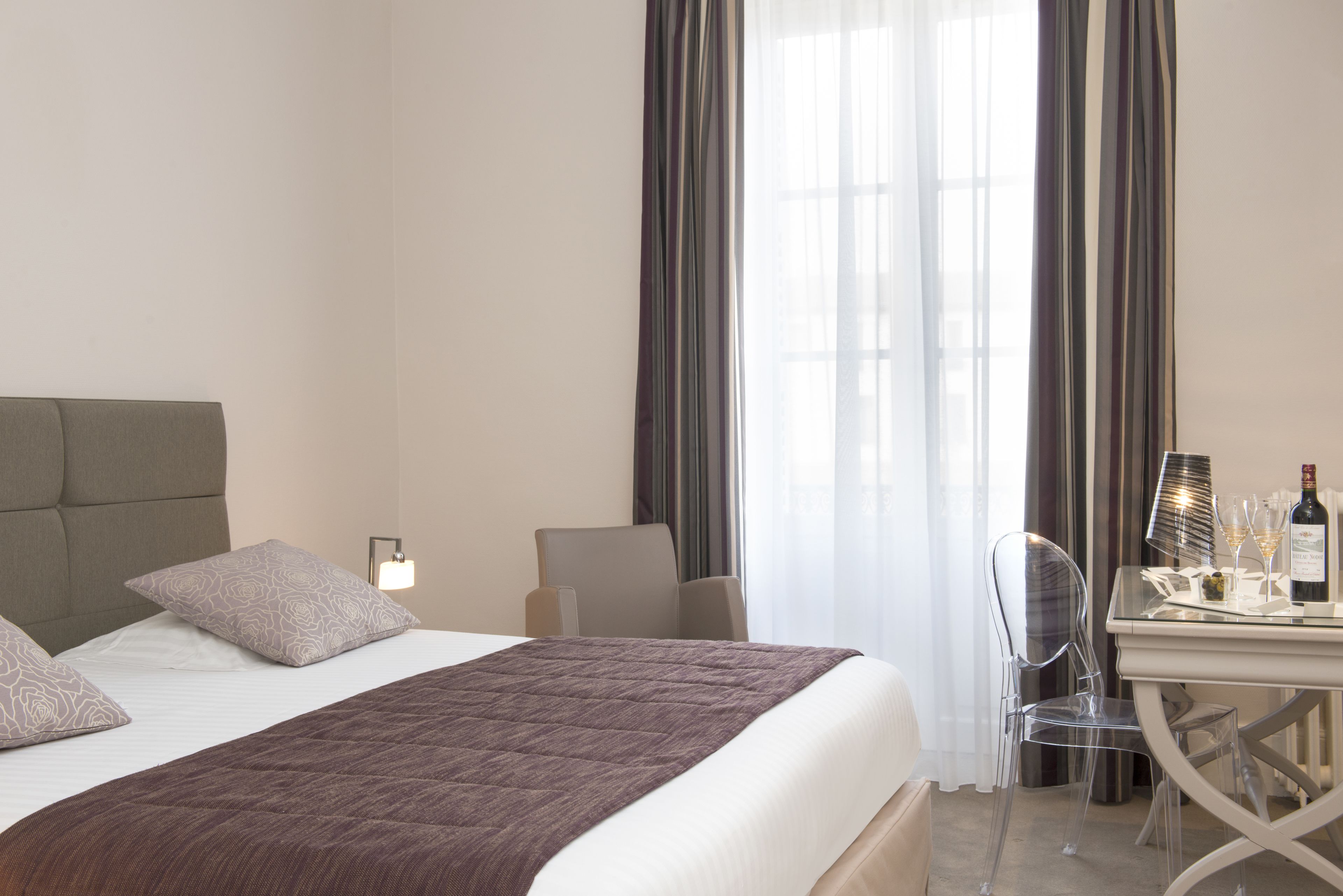 A hotel room with a bed, a desk with a chair, a bottle of wine, and glasses.
