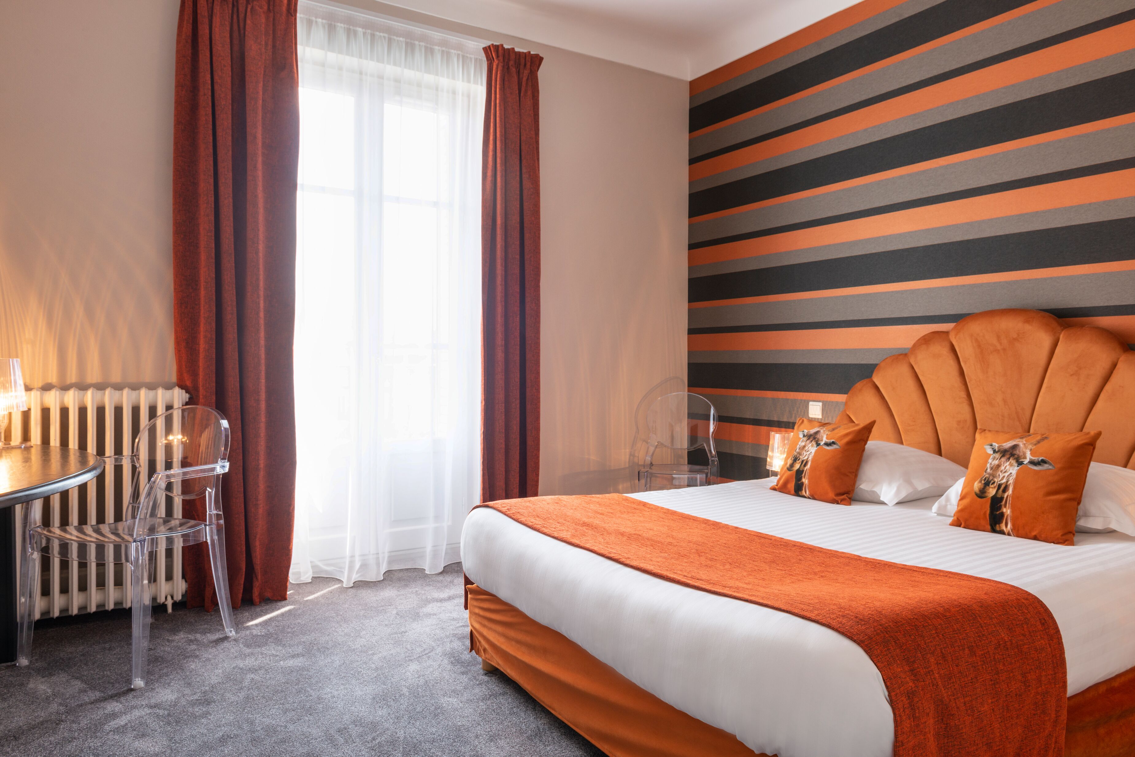 A hotel room with a large bed, a dining table with chairs, a radiator, and a window with curtains.