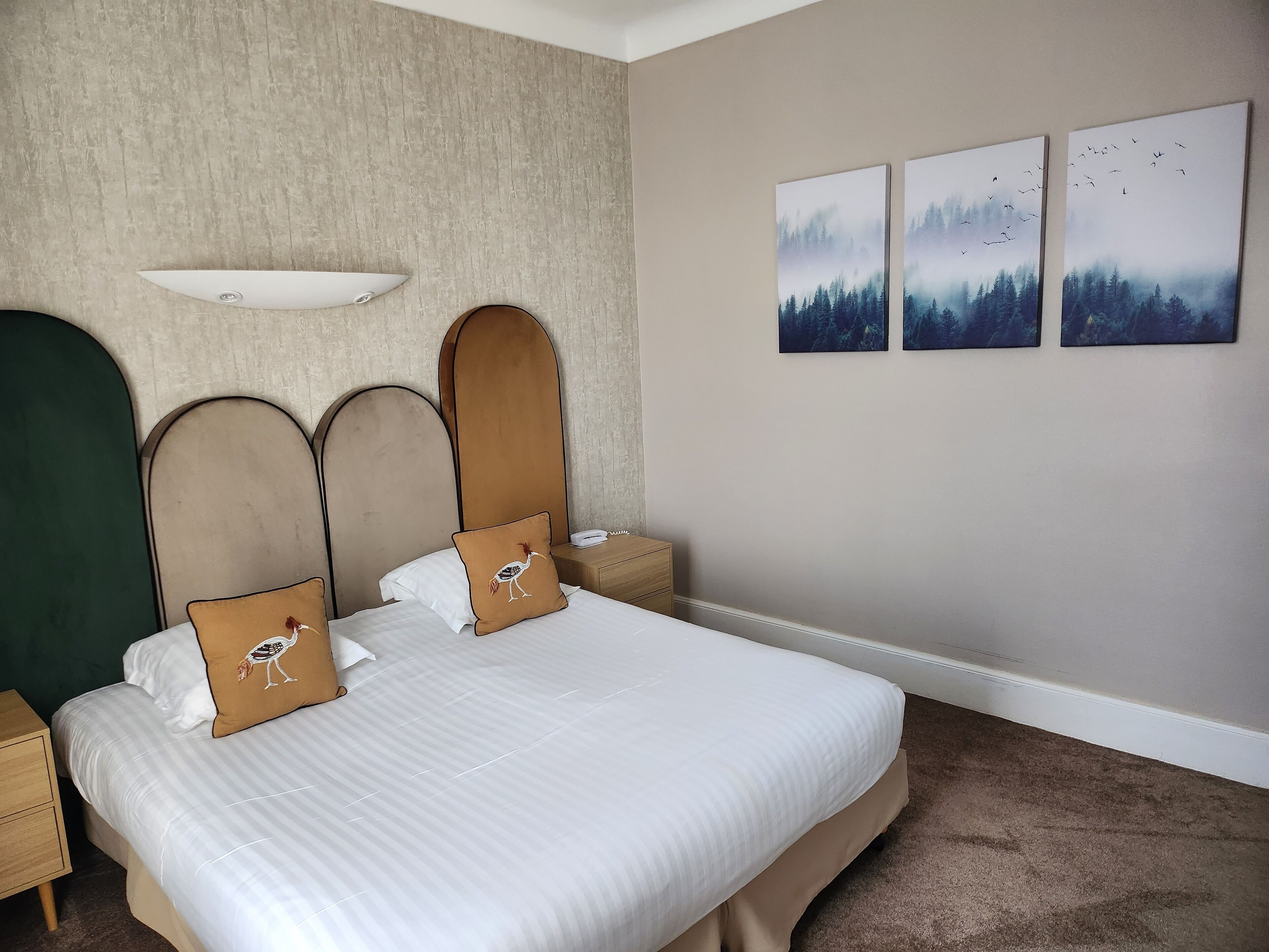 A hotel room with a large bed, two nightstands, a wall-mounted lamp, and three framed pictures.