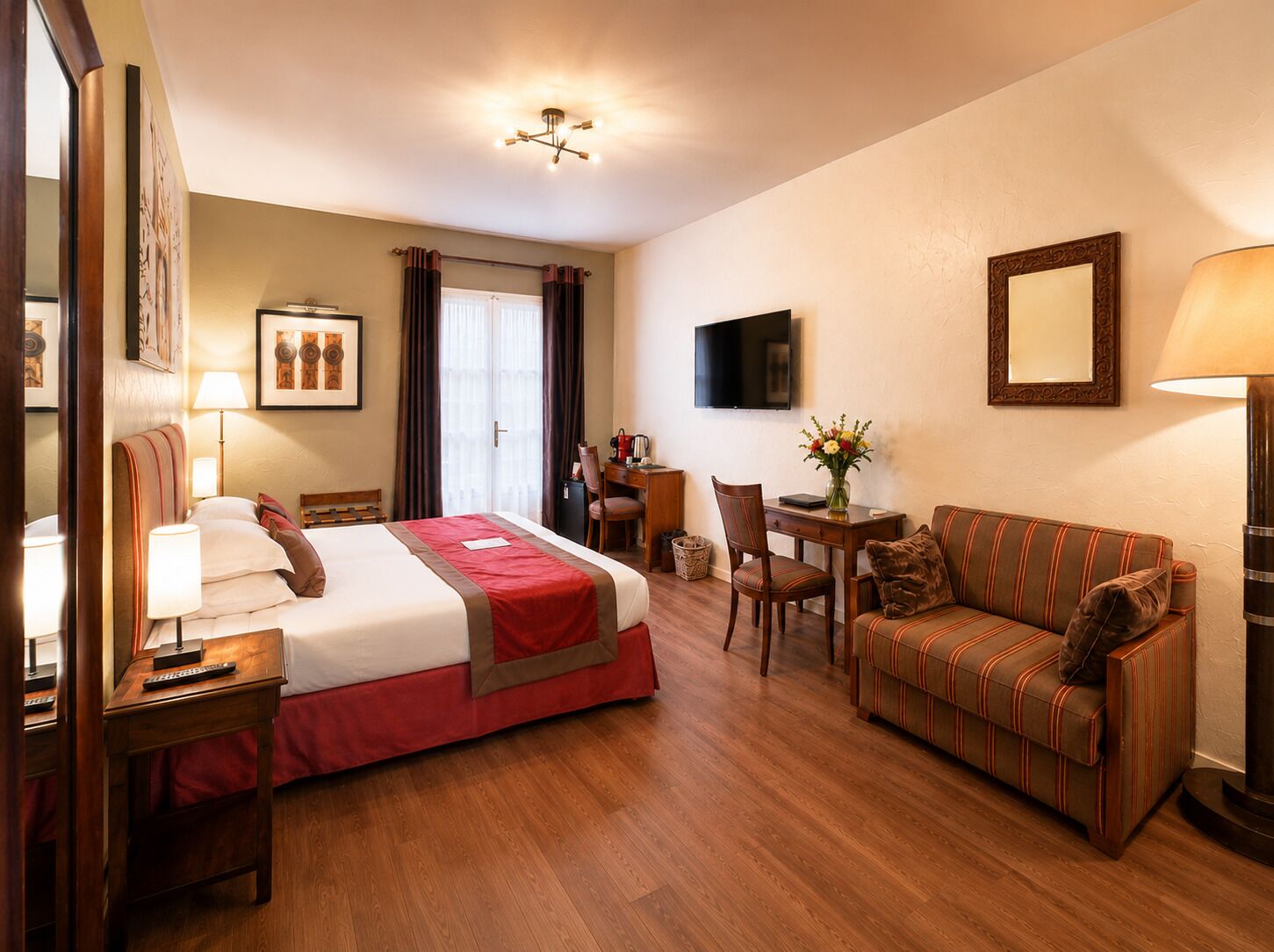 A hotel room with a bed, a sofa, a desk, a television, and a lamp.