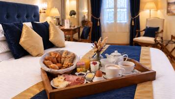 Une chambre d’hôtel avec un plateau de petit-déjeuner soigneusement préparé sur le lit, comprenant des viennoiseries, du fromage et des boissons.
