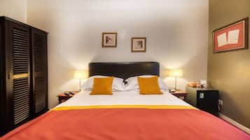 A hotel room with a large bed, two bedside lamps, a nightstand, a wooden wardrobe, and two framed pictures on the wall.