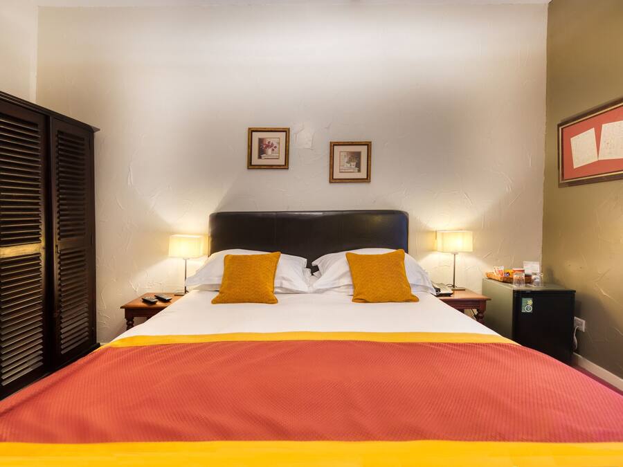 A hotel room with a large bed, two bedside lamps, a nightstand, a wooden wardrobe, and two framed pictures on the wall.