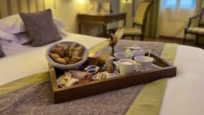 A hotel room with a neatly made breakfast tray on the bed, including various pastries, cheeses, and cups.