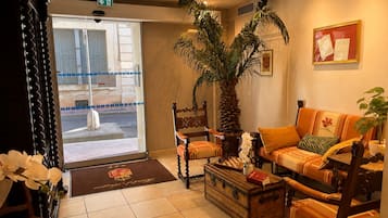 A hotel lobby with a reception desk, a palm tree, a sofa, and a chessboard.