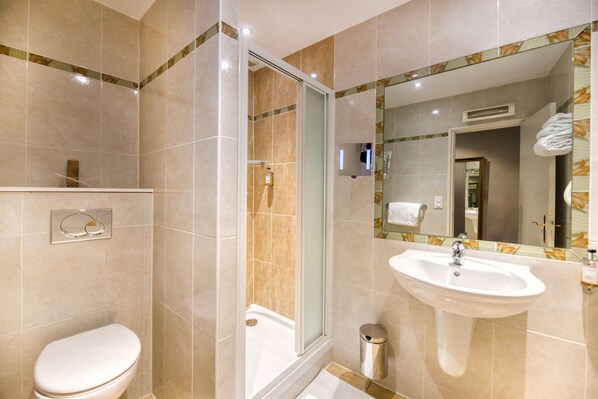 Un baño con inodoro, ducha, lavabo y espejo con marco decorativo.