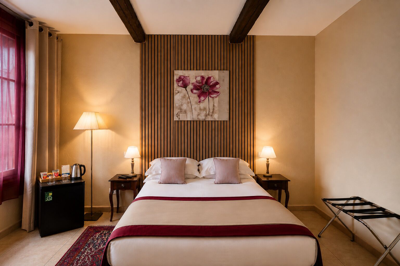 A hotel room with a large bed, two bedside tables, a wall-mounted artwork, a red throw blanket, a coffee machine, and a hanging laundry rack.