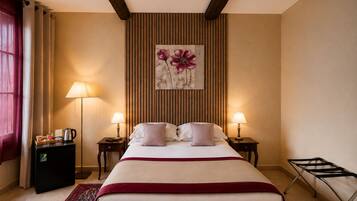 A hotel room with a large bed, two bedside tables, a wall-mounted artwork, a red throw blanket, a coffee machine, and a hanging laundry rack.