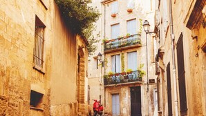 A narrow street with a red scooter parked on the side, buildings with balconies, and a sign that reads 'Hotel'.