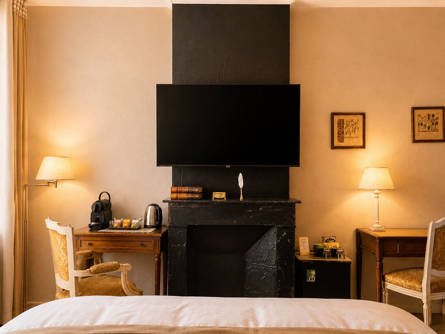 A hotel room with a bed, a desk with a chair, a fireplace, a television, and two lamps.