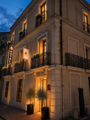 Fachada de hotel con un cartel que indica que es un establecimiento de 4 estrellas, con balcones ornamentados con plantas, estilo arquitectónico clásico y una entrada acogedora.